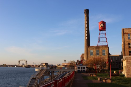Historic Fitger's Brewery building with a tall smokestack and water tower, alongside a scenic waterfront path.