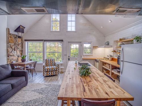 Bright, modern kitchen with wooden dining table, cozy seating, and large windows showcasing a scenic view.