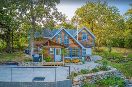 A charming wooden house with blue accents, surrounded by greenery and colorful flowers in a serene outdoor setting.