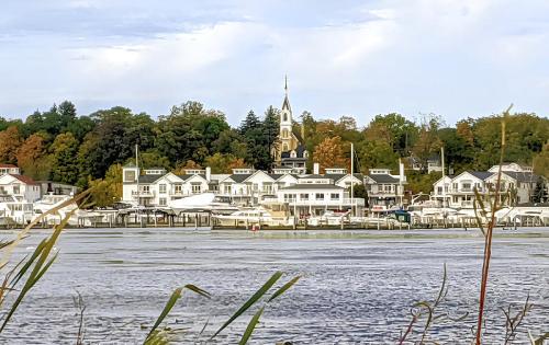A scenic view of a riverside town with a church steeple, surrounded by trees and boats along the water.