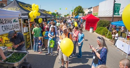 A lively street fair with vendors, colorful tents, and people enjoying the festivities, some holding yellow balloons.