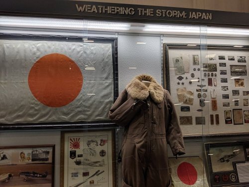 Display featuring a Japanese flag, military artifacts, and a fur-lined flight jacket under the title "Weathering the Storm: Japan."