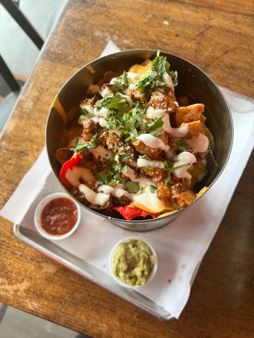 A bowl of nachos topped with chicken, cheese, cilantro, and drizzled with sauce, served with salsa and guacamole.