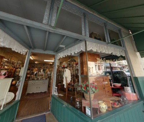 A vintage shop entrance with lace curtains, showcasing various antiques and collectibles inside.