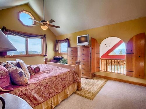 Cozy bedroom with a large bed, dresser, and windows offering scenic views, featuring warm colors and a ceiling fan.