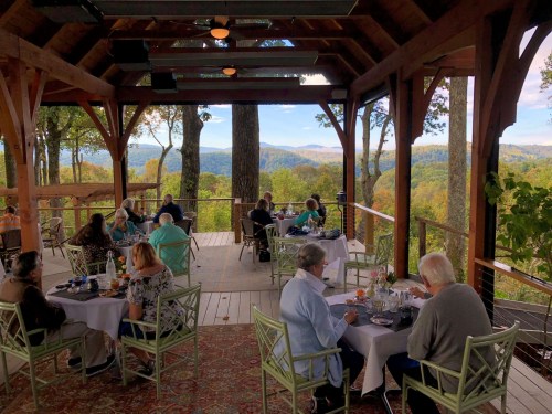 A scenic restaurant patio with diners enjoying a view of mountains and trees in a vibrant autumn setting.