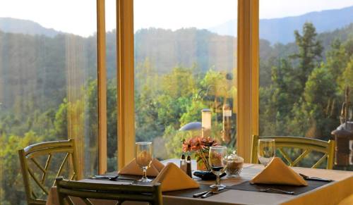 A beautifully set dining table with mountain views through large windows, featuring flowers and elegant tableware.
