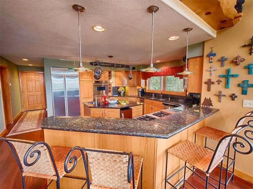 Modern kitchen with wooden cabinets, granite countertops, and bar seating, featuring colorful wall decor and large windows.