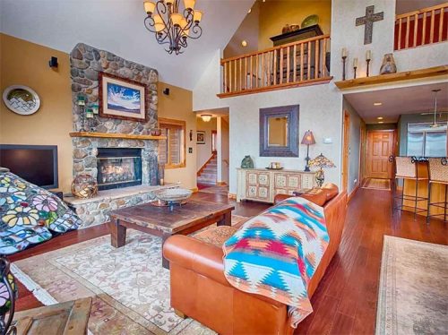 Cozy living room with a stone fireplace, wooden accents, and a colorful blanket draped over a leather sofa.