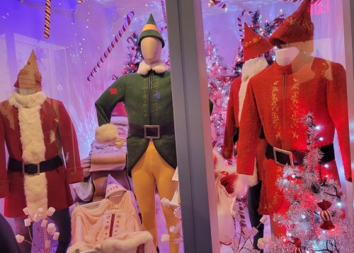 Display of festive holiday costumes, including Santa, an elf, and Christmas-themed outfits, surrounded by decorations.