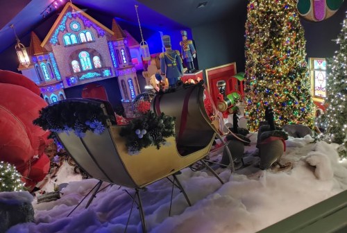 A festive scene featuring a decorated Christmas tree, a sleigh, and holiday decorations in a snowy setting.