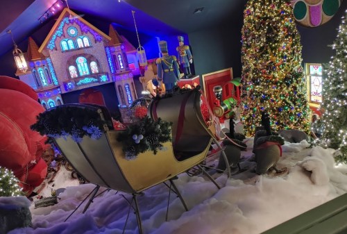 A festive scene featuring a decorated sleigh, Christmas trees, and colorful holiday decorations in a cozy room.