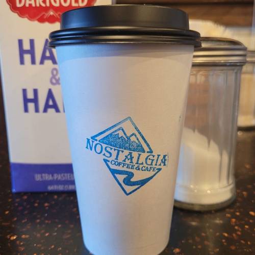 A coffee cup with a logo from Nostalgia Coffee & Café, next to a carton of milk and a sugar jar.