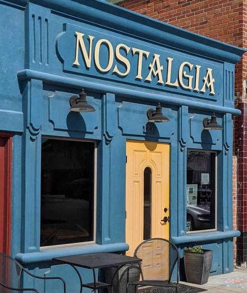 A vibrant blue storefront with the word "NOSTALGIA" in bold letters and a yellow door, featuring outdoor seating.