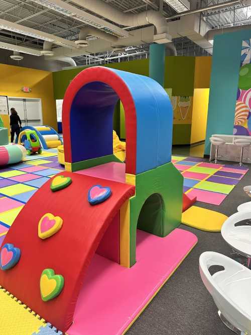 Colorful play structure with a slide, surrounded by soft mats in a bright indoor play area for children.