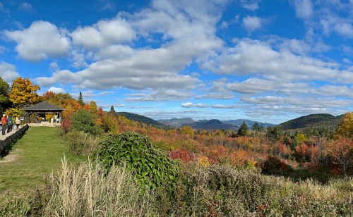 A scenic view of colorful autumn foliage with mountains in the background and a cloudy blue sky.
