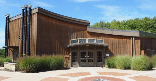 A modern wooden building with large windows, surrounded by greenery and a circular stone pathway.