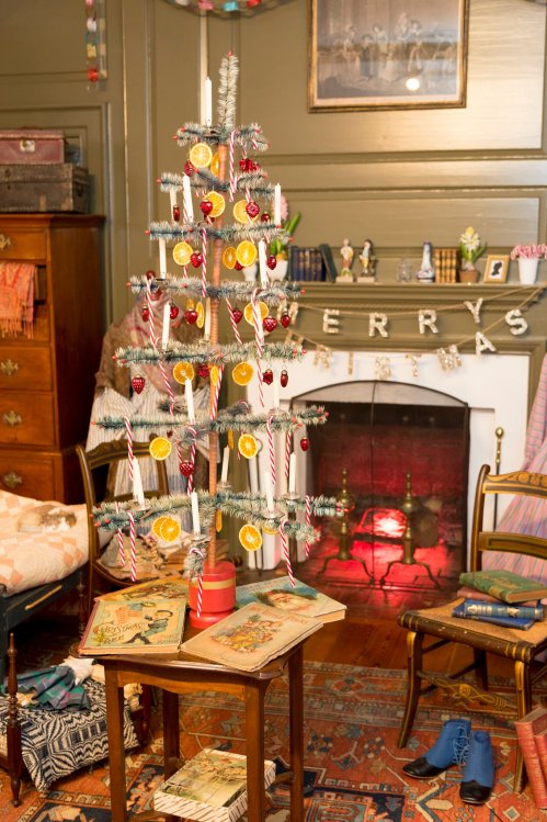 A decorated Christmas tree with orange slices and candy canes, beside a cozy fireplace and vintage books in a festive room.