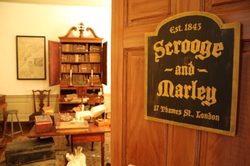 Sign reading "Scrooge and Marley, Est. 1843, 17 Thames St., London" in a vintage office setting with bookshelves.