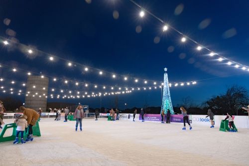 People ice skating at night under string lights, with a decorated Christmas tree in the background.