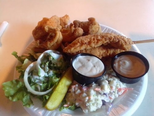 A plate of fried fish, coleslaw, lettuce, pickles, and two dipping sauces.