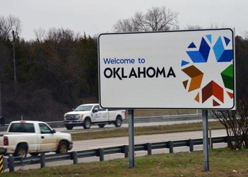 Welcome sign for Oklahoma with a colorful star design and vehicles passing by on the highway.