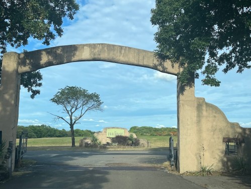 A stone archway leads to a grassy area with trees under a blue sky, creating a serene entrance.