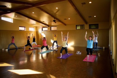 A group of people practicing yoga in a spacious, well-lit studio with wooden beams and colorful mats.