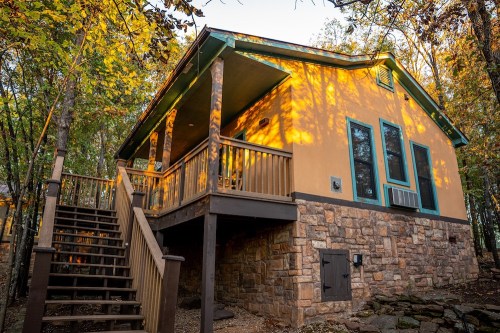 A cozy cabin with a stone foundation, wooden stairs, and vibrant autumn foliage surrounding it.