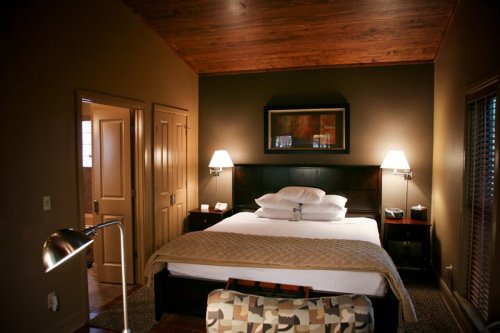 Cozy bedroom with a wooden ceiling, a large bed, bedside lamps, and a warm color palette.