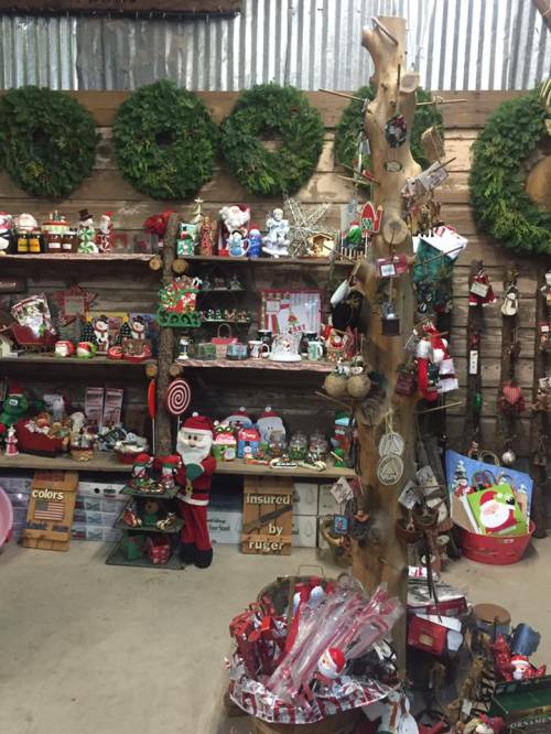 A festive display of Christmas decorations, including wreaths, ornaments, and Santa figurines in a rustic shop.
