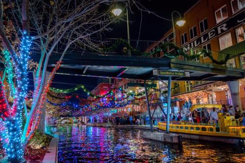 A vibrant canal scene at night, adorned with colorful lights and festive decorations, bustling with people and boats.