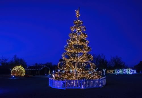 A beautifully lit Christmas tree with swirling lights, surrounded by festive decorations against a twilight sky.