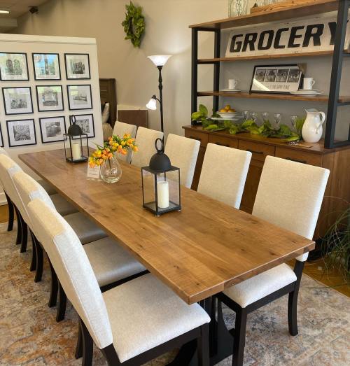 A spacious dining area with a long wooden table, white chairs, and decorative items on a shelf and table.