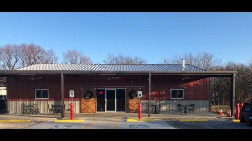A red barn-style building with a metal roof, featuring a welcoming entrance and outdoor seating.