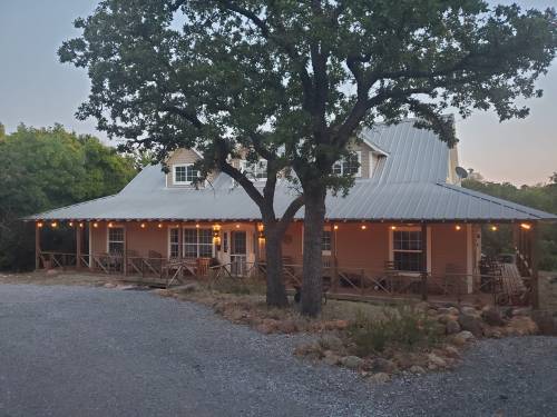 A charming house with a metal roof, surrounded by trees and gravel, illuminated by string lights in the evening.