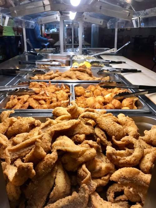 A buffet display featuring trays of crispy fried fish and shrimp, with lemon slices in the background.