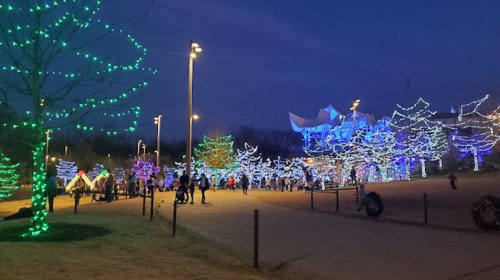 A park illuminated with colorful holiday lights, featuring trees and people enjoying the festive atmosphere at night.