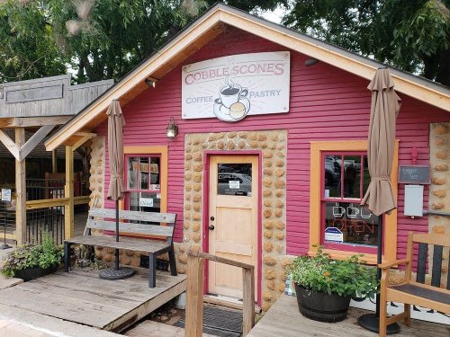 A colorful coffee and pastry shop with a stone facade and a sign reading "Cobble Scones," featuring outdoor seating.