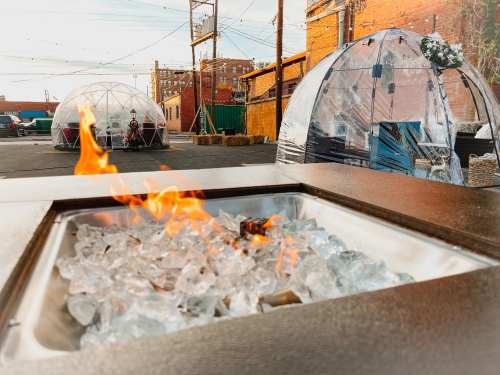 A fire pit with glass stones in the foreground, with transparent domes and people sitting in the background.