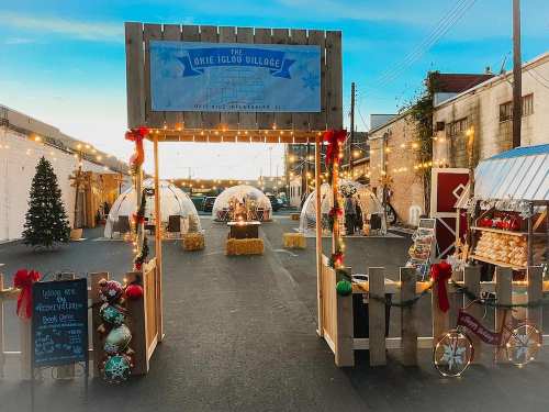 A festive outdoor village with igloos, holiday decorations, and a Christmas tree, illuminated by string lights.
