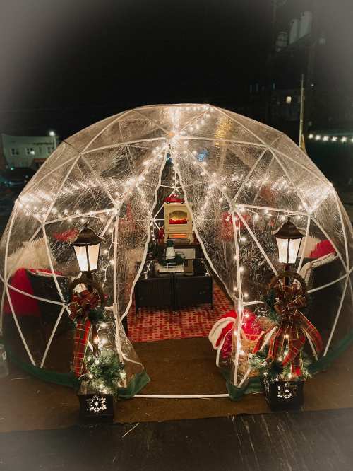 A festive outdoor igloo decorated with lights, lanterns, and holiday decor, creating a cozy winter atmosphere.
