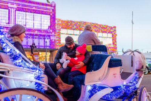 A family enjoys a festive carriage ride, surrounded by colorful holiday lights and decorations.