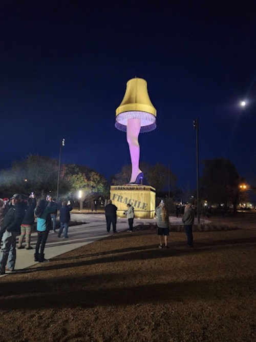 A large, illuminated lamp statue with a yellow shade stands at night, surrounded by a crowd of people.