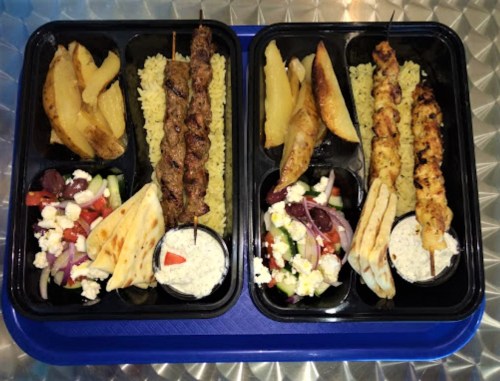 Two meal trays with skewers of meat, rice, potatoes, salad, and pita bread, served on a blue tray.