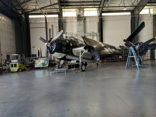 A vintage aircraft in a hangar, with propellers and a sleek black design, surrounded by tools and equipment.