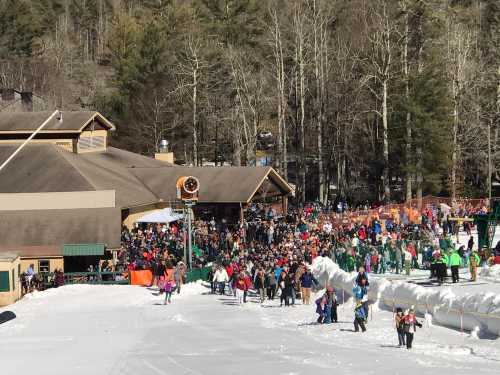 A crowded ski resort with people walking in the snow, surrounded by trees and a lodge in the background.