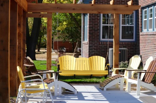 A cozy outdoor seating area with yellow and brown Adirondack chairs under a wooden pergola.