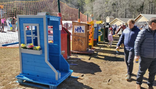 A colorful wooden structure resembling a small house, with people walking by in a snowy outdoor setting.