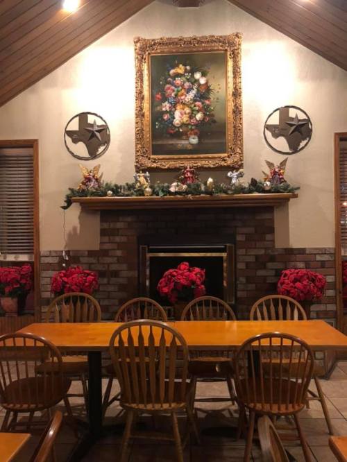 Cozy dining area with a wooden table, chairs, and a decorated fireplace featuring a floral painting and festive poinsettias.